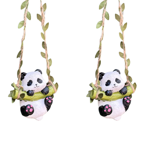 Two cute panda figurines sitting on bamboo swings, suspended by twine ropes decorated with artificial green leaves. The pandas feature pink paw pads and a hand-painted resin finish against a white background.