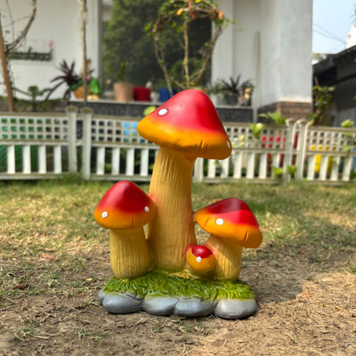 A colorful garden statue featuring three red-capped mushrooms of varying heights on a green mossy base, set against a blurred backyard fence.