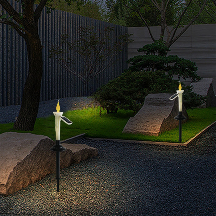 Two solar-powered candle garden stakes emitting a warm flickering glow along a gravel path at dusk