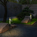 Two solar-powered candle garden stakes emitting a warm flickering glow along a gravel path at dusk