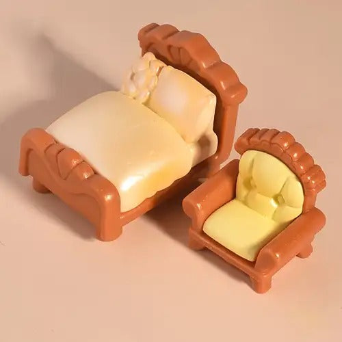 Two-piece miniature dollhouse furniture set featuring a brown carved bed with cream bedding and a matching upholstered armchair.