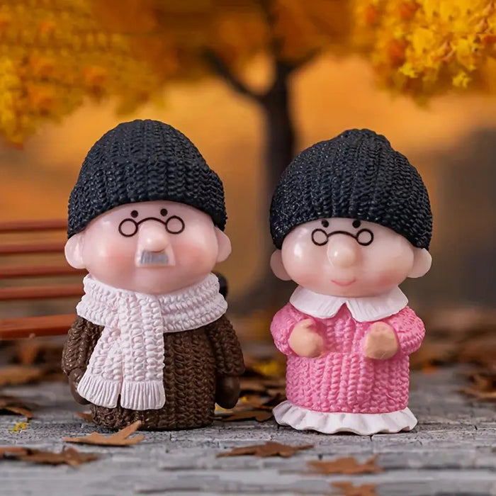 Elderly couple miniature figurines in knit hats and winter clothing, standing among autumn leaves.