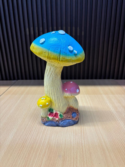 A whimsical trio mushroom garden statue featuring a large blue cap, a medium pink cap, and a small yellow cap, all with white spots and realistic textured stems on a rocky base with tiny red flowers.