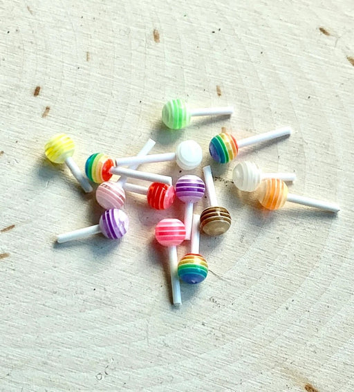 colorful striped lollipop miniature charms with white sticks, scattered on a distressed light wood surface.