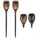 A decorative black solar torch light with an intricate cutout pattern glowing with an orange flickering flame effect against a white garden fence at night.