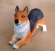 dog toy statue. The toy is orange, black, and white and is lying down on a brown table.