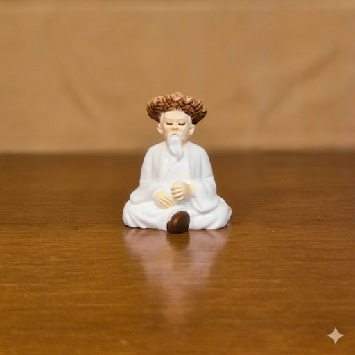 Miniature resin figurine of an elderly Chinese monk or sage with white robes and curly brown hair, seated in a meditative position on a wooden table.