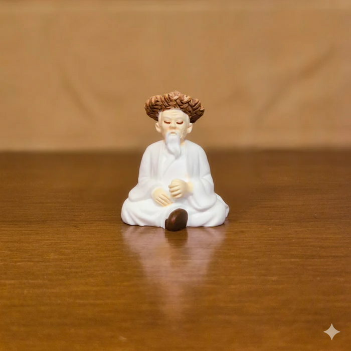 Miniature resin figurine of an elderly Chinese monk or sage with white robes and curly brown hair, seated in a meditative position on a wooden table.