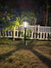 "Black solar-powered garden pathway light glowing at night in front of a white lattice fence and green bushes."