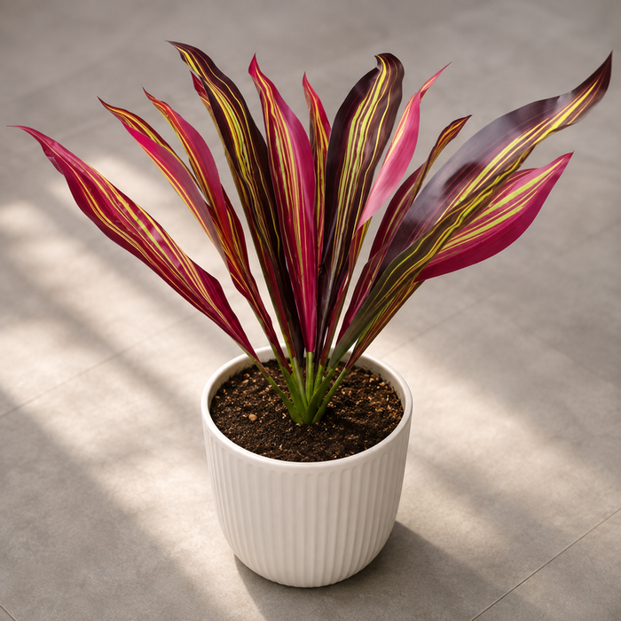 Artificial tropical plant with vibrant red and yellow striped leaves planted in a white ribbed pot on a grey tiled floor