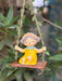 A whimsical garden figurine of a young girl with a floral crown and yellow dress sitting on a wooden swing suspended by leaf-entwined twine.