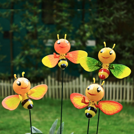 Four cute, smiling honey bee garden stakes with bright orange and yellow bodies and colorful wings, standing in a garden with a blurred fence background.