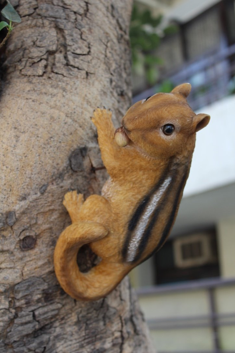 Resin climbing chipmunk garden statue mounted on a tree trunk holding a nut.