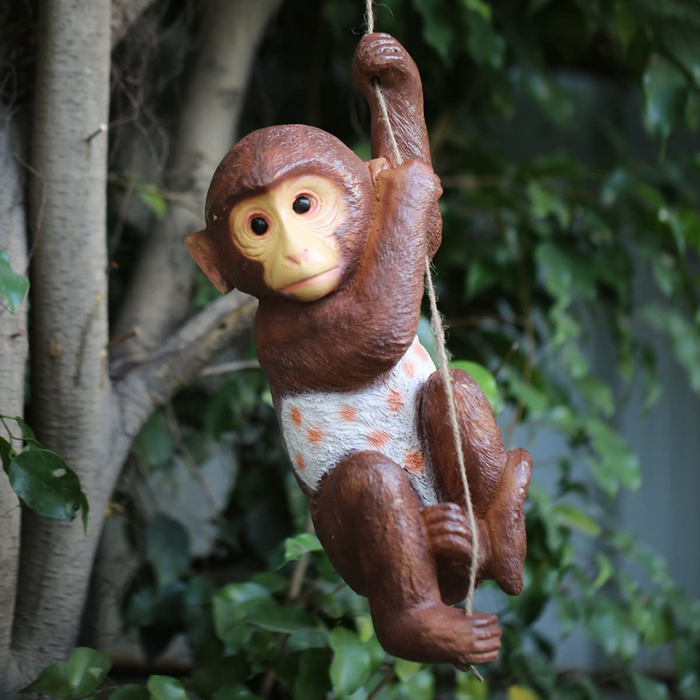 A brown hanging monkey garden statue wearing a white and orange polka-dot diaper, clutching a rope