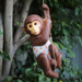 A brown hanging monkey garden statue wearing a white and orange polka-dot diaper, clutching a rope