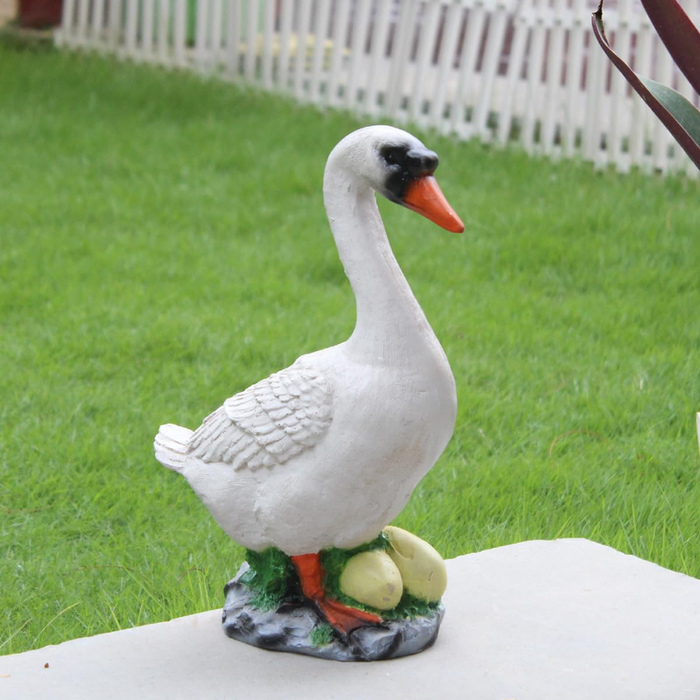 A hand-painted white duck and nest with eggs garden statue standing outdoors on a stone surface with green grass