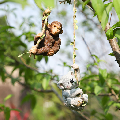 Two realistic resin garden animal figurines—a brown monkey and a grey koala—hanging from a tree branch by jute ropes with green leaf accents against a blurred garden background.
