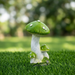 Handpainted green resin mushroom garden statue with white spots resting on lush green grass for outdoor lawn and yard decor