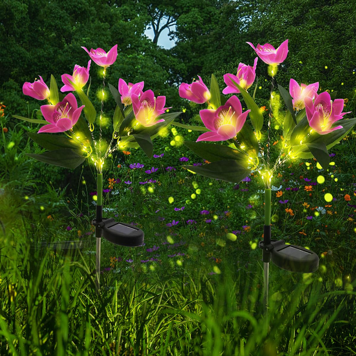 Two solar-powered pink lotus flower garden stakes with glowing yellow firefly lights installed in a green lawn