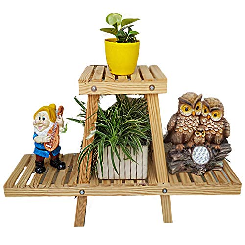 A two-tier light wood plant stand featuring a slatted design, shown holding a yellow potted plant, a spider plant, a gnome figurine, and an owl statue.