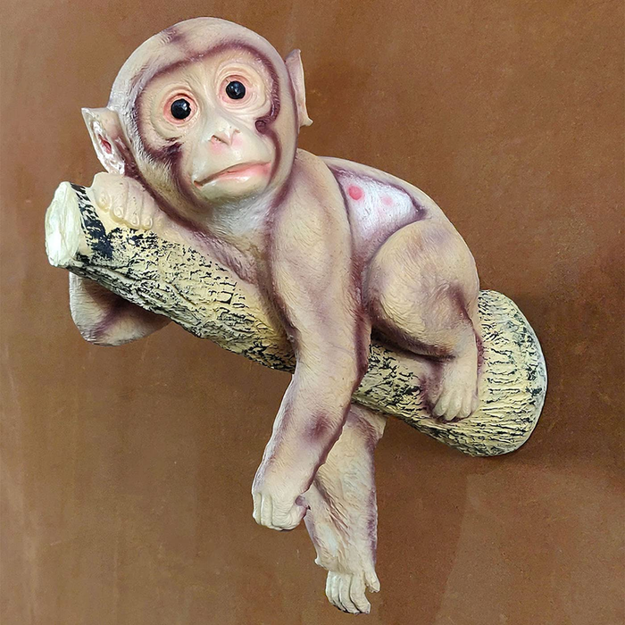 A detailed resin figurine of a cute baby monkey resting and hanging over a textured tree branch against a warm brown background