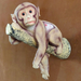 A detailed resin figurine of a cute baby monkey resting and hanging over a textured tree branch against a warm brown background