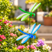 Set of 2 colorful green and blue dragonfly garden stakes with translucent wings in a flower garden