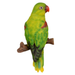 A lifelike figurine of a green parrot with a red beak and maroon wing patches, perched on a short brown branch, isolated on a white background.