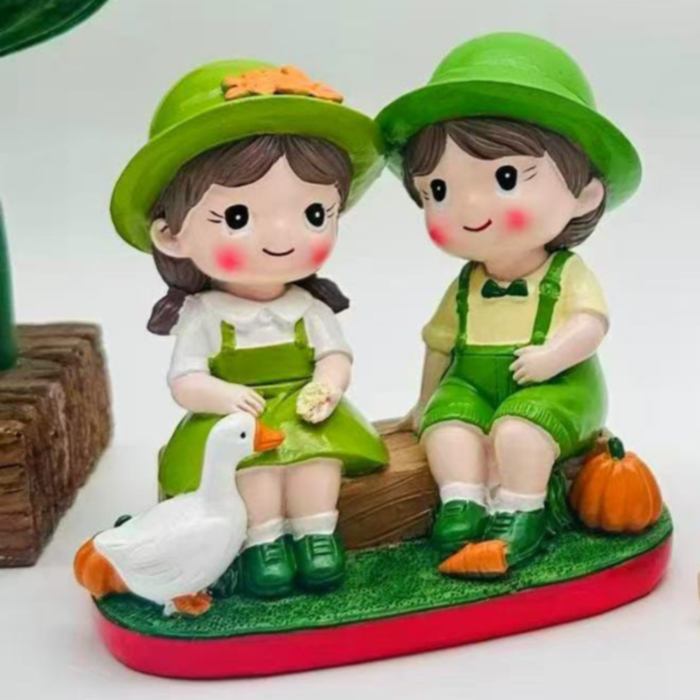 Hand-painted figurine of a young boy and girl in green garden outfits sitting on a log with a white duck and a small orange pumpkin.