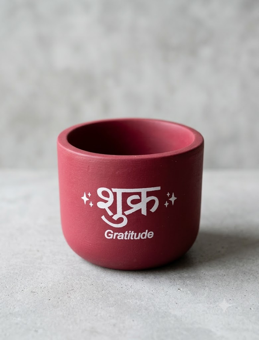 Handmade maroon terracotta plant pot featuring the word "Shukr" (gratitude) in white script with small star accents on a grey background.