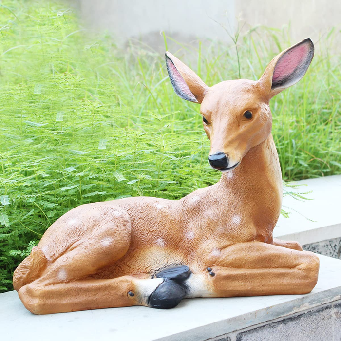 A realistic reclining fawn garden statue resting on a ledge