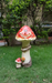 A colorful garden statue of a large red-and-white capped mushroom with a happy face, a smaller mushroom, and a snail