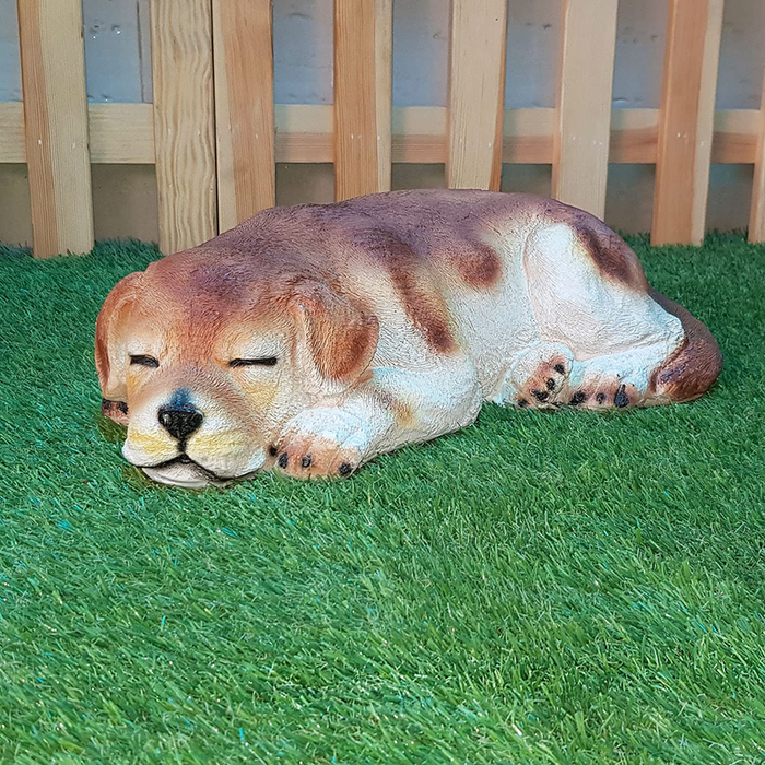 A realistic sleeping dog resin garden statue resting on green artificial turf
