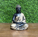 Small black and gold Buddha statue sitting in a meditative dhyana mudra pose on a wooden surface against a green grass background.