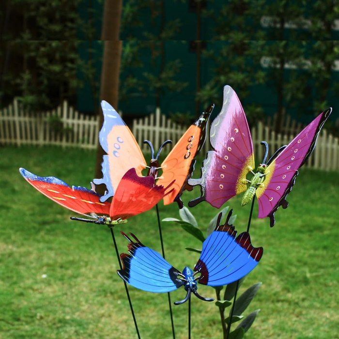 A group of colorful metal butterfly stakes in shades of blue, purple, orange, and red, standing on thin wire stems in a green grassy garden.