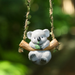Cute grey koala figurine sitting on a wooden-style hanging swing holding green leaves, ideal for fairy garden accessories and miniature decor.