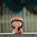 A miniature resin planter shaped like a girl’s head with a flower crown and her finger to her lips in a shushing gesture, set against a blurred garden background.