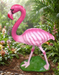 Decorative pink flamingo garden statue with a textured green base standing on a grey floor