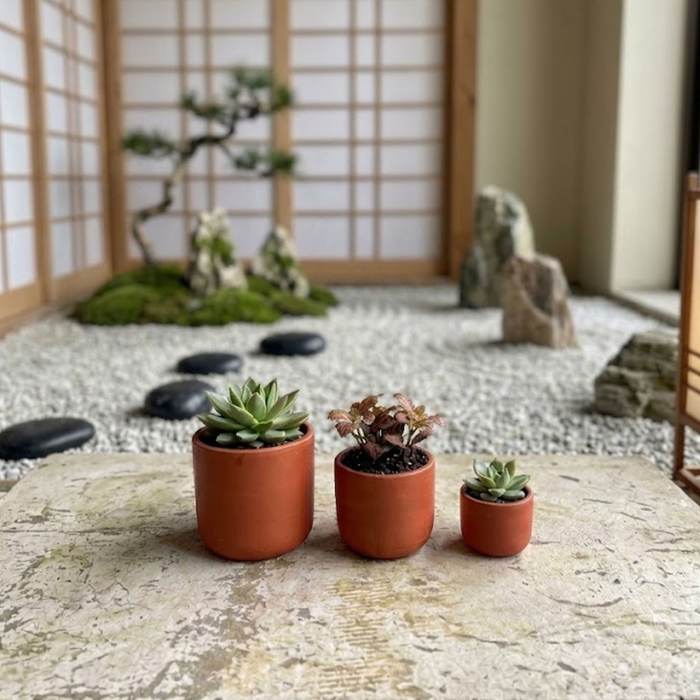 Set of three minimalist handmade terracotta planter pots in graduated sizes arranged on a white background
