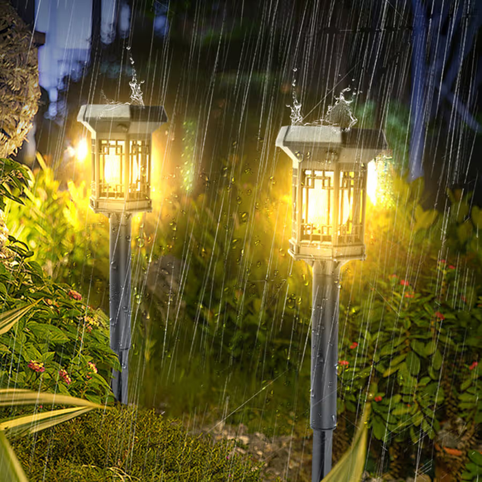 Two vintage-style solar pathway lights glowing brightly along a garden path during rainfall