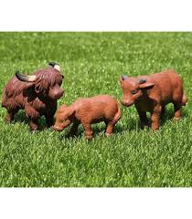Three realistic plastic farm animal figurines—a shaggy adult Highland cow, a smaller brown cow, and a calf—standing on vibrant green artificial grass.