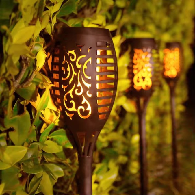 Set of four black solar-powered garden torch lights with decorative lattice cutouts and glowing orange flickering flame LED effect.