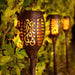 Set of four black solar-powered garden torch lights with decorative lattice cutouts and glowing orange flickering flame LED effect.