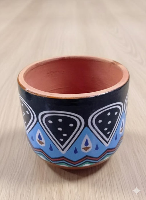 A small, round terracotta planter painted with a bold, tribal-inspired pattern in black, white, and various shades of blue.