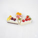 Set of 3 realistic non-edible cake slices with assorted fruit toppings (cherries, strawberries, blueberries, peaches) for decorative display or photography props.