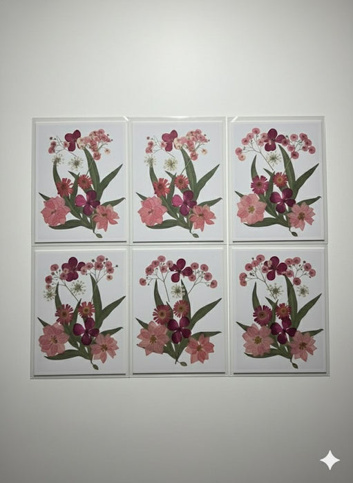 A close-up image of a handcrafted art piece featuring a bouquet arrangement of real, pressed pink and red flowers, including zinnias and baby's breath, sealed on a white background.