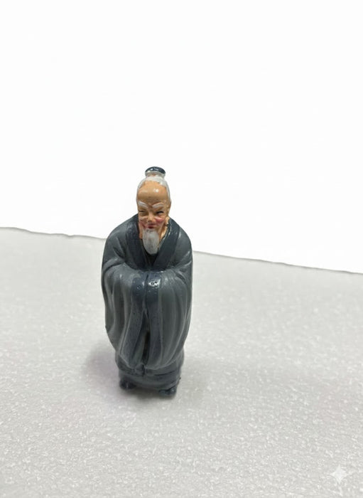 Small statue of an old Chinese monk with a white beard and a dark gray robe.