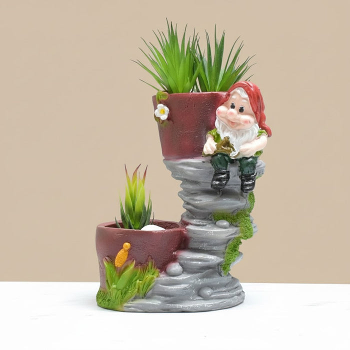 Two-tier ceramic planter shaped like a gray rock formation with a smiling garden gnome figure wearing a red hat sitting on the upper ledge. The planter holds artificial spiky green succulent plants."