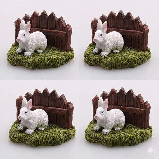 Four white miniature resin rabbit figurines sitting on green grass in front of a small brown wooden fence.