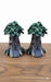 Pair of dark grey miniature fairy garden tree stump houses with green leafy roofs, tiny arched doors, and stone steps